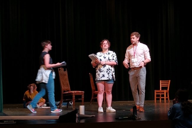 A group of youth are on stage rehearsing for a musical production.