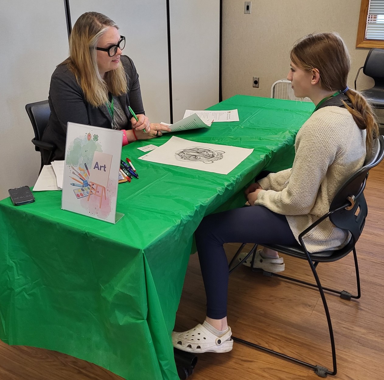 Youth and adult sit on opposite sides of a table with a green cloth having a discussion.