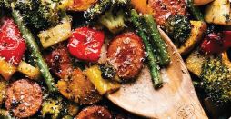 Skillet full of cooked sausage and vegetables with a wooden spoon on the side.