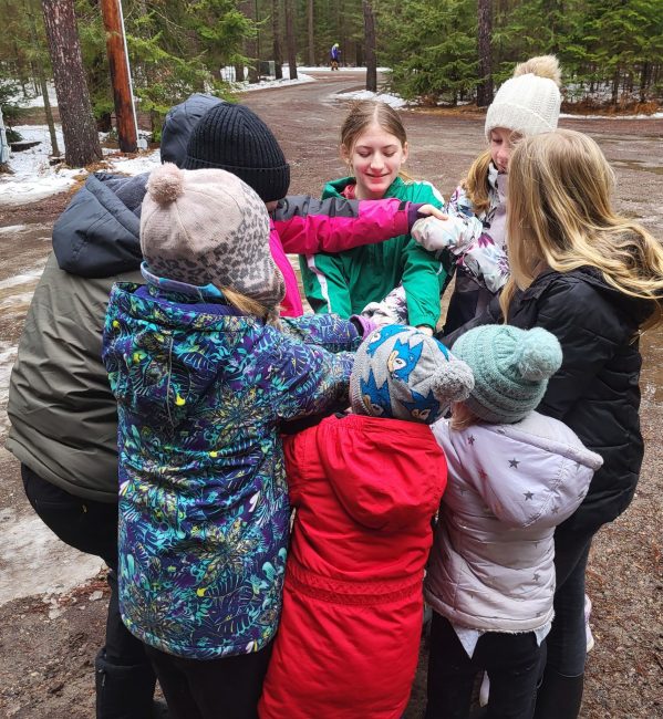 A group of youth huddle together in a circle outside in winter and hold hands.