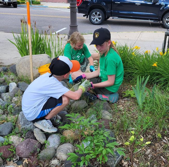 Three youth plant flowers in a small garden.