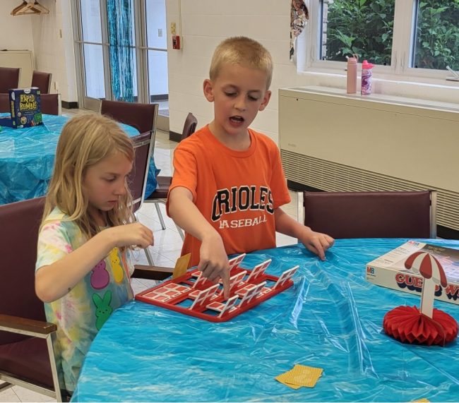 Two youth play the game "Guess Who" at a table together.