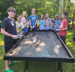 A group of youth surround a table they built and are now painting black.