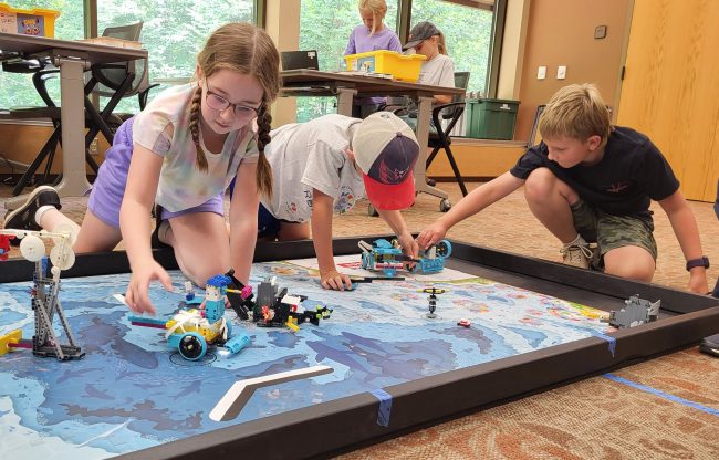 Three youth setting up Lego robots on the floor.