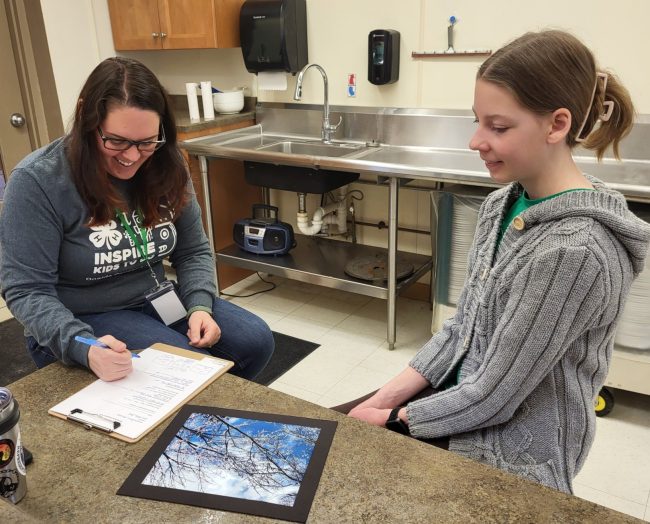 A girl and adult sit at a counter and discuss the work of art the child created for the expo.