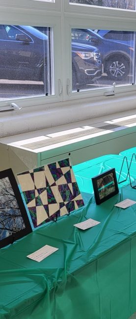 Art is displayed on a long table with a green tablecloth.