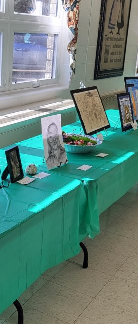 Art is displayed on a long table with a green tablecloth.