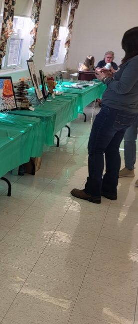 Art is displayed on a long table with a green tablecloth.