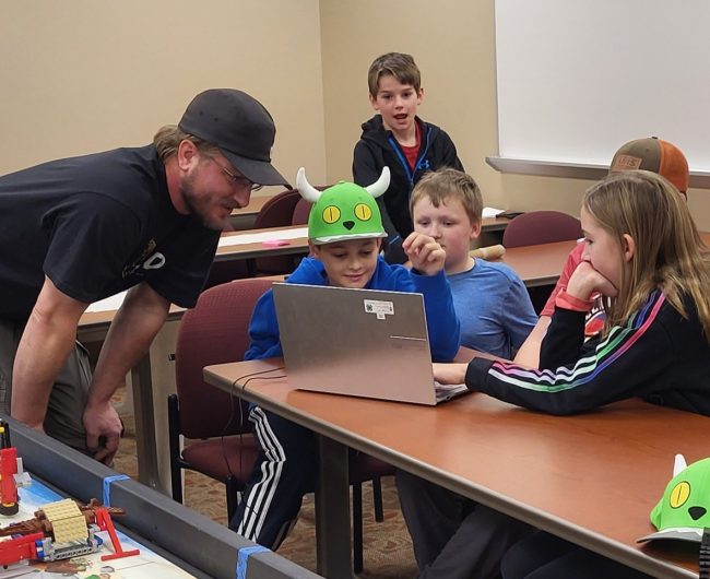 An Oneida County 4-H volunteer looks at a laptop with youth in the Lego Robotics Club during a meeting.