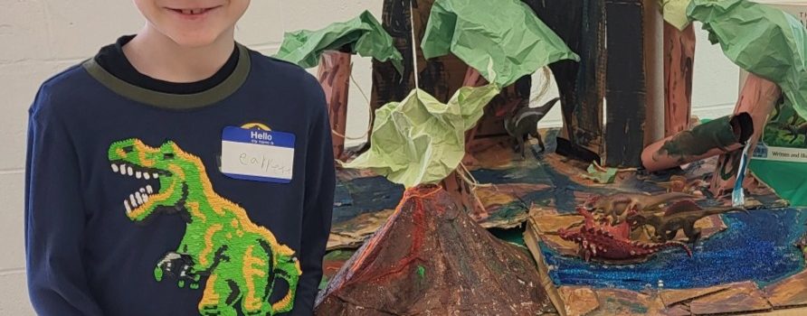 A young boy stands in front of a dinosaur art project he made for the expo.