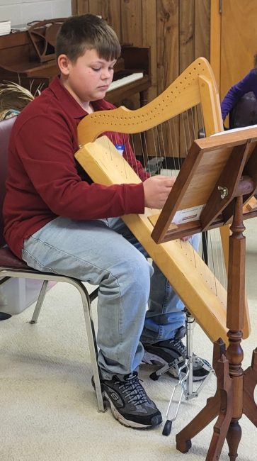 A child sits on a chair while playing a string instrument.
