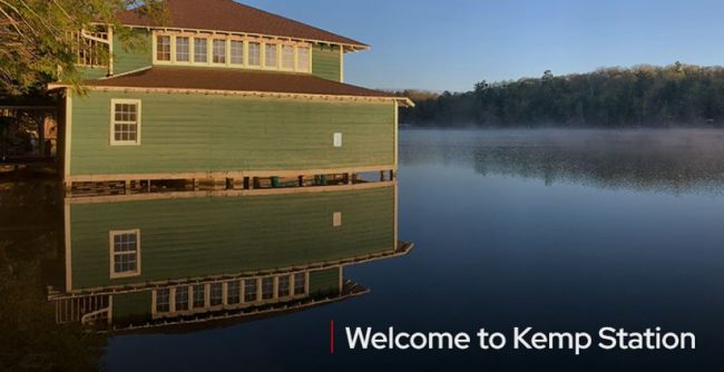 Photo of green house with stilts sitting on a lake surrounded by trees. It states 'Welcome to Kemp Station".