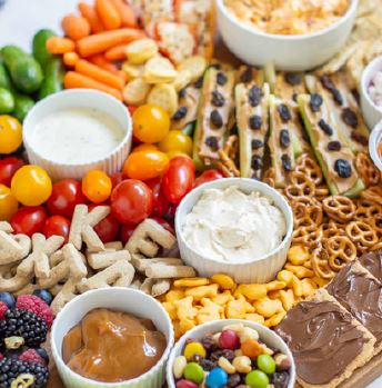 A tray full of health snacks, such as cherry tomatoes, pretzels, baby carrots, trail mix, and berries.