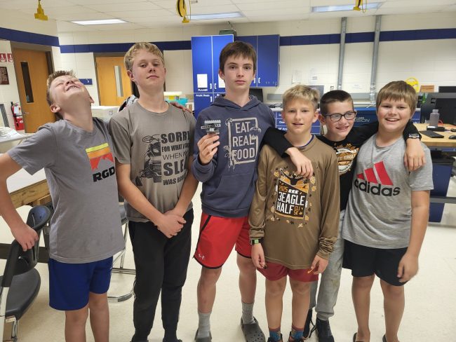 A group of six boys stand side by side in a line and smile for the camera.