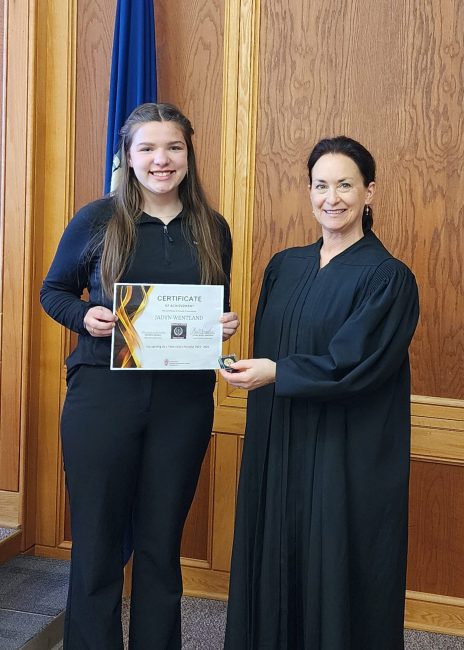 A Teen Court panelists stands side-by-side with a judge holding up a certificate during a pinning ceremony.