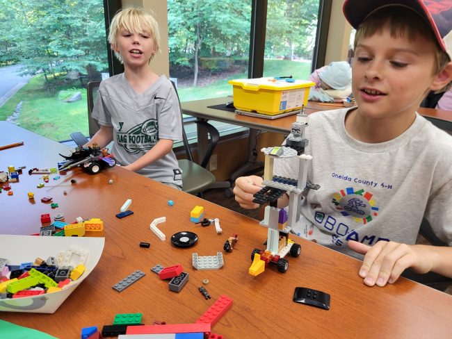 Two youth sit at a table and put together Legos to build a robot.